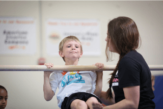 A boy is instructed on a horizontal bar in a kids gymnastics class.