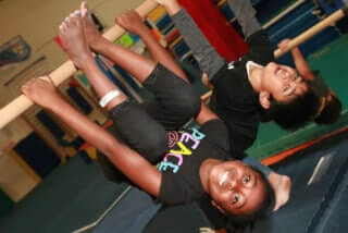 A girl and a boy hang upside down, smiling ear to ear, on a horizontal bar.