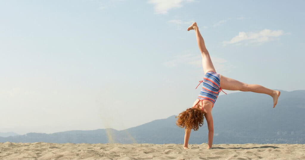 Girl doing cartwheels in sand on the beach