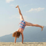 Girl cartwheels on the beach, thumbnail.