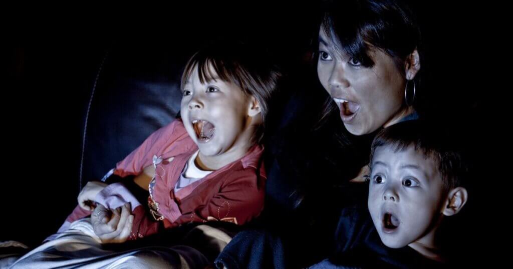 Family sitting on couch, looking surprised while lit from movie screen